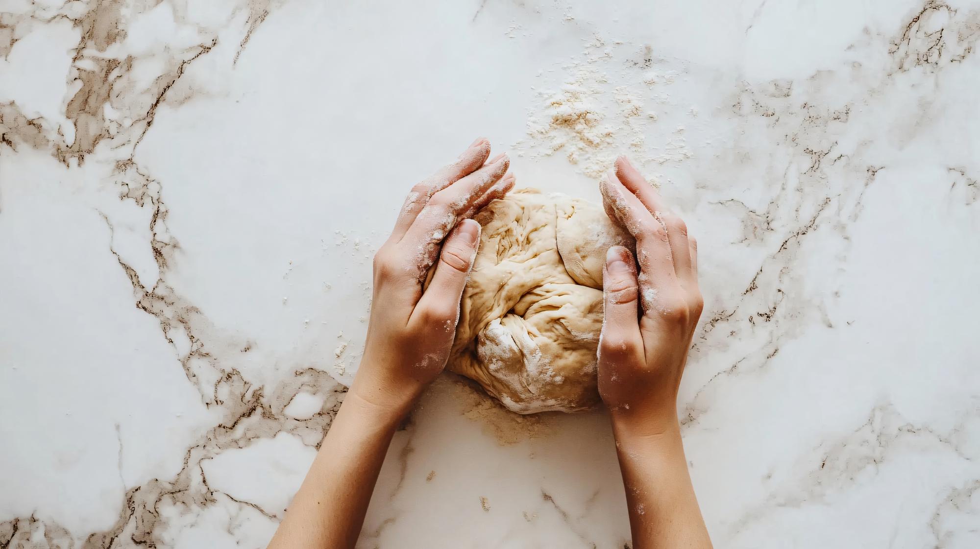 Hands kneading dough on marble surface